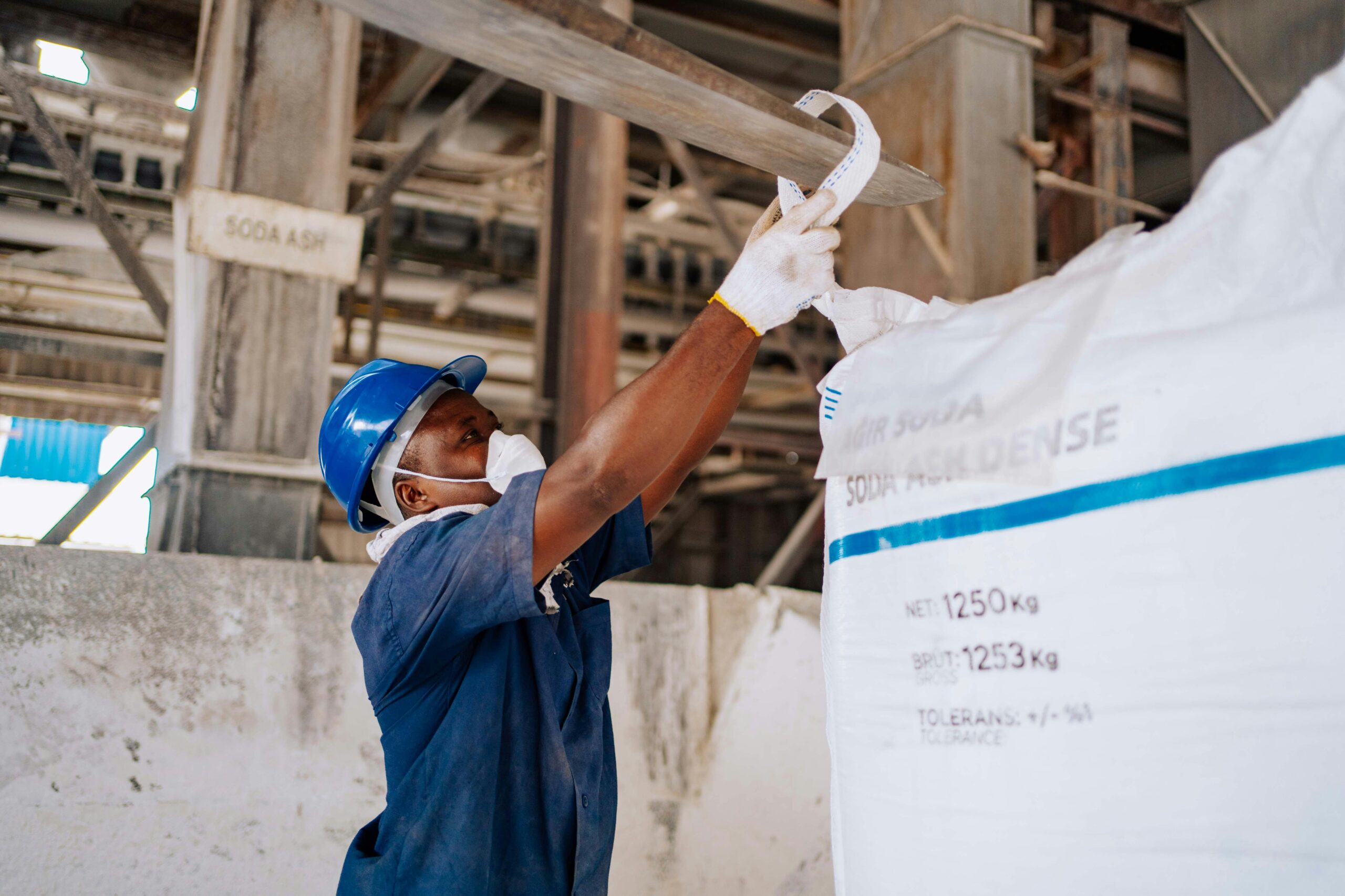 Industrial worker checking a large soda ash bag in a manufacturing facility.
