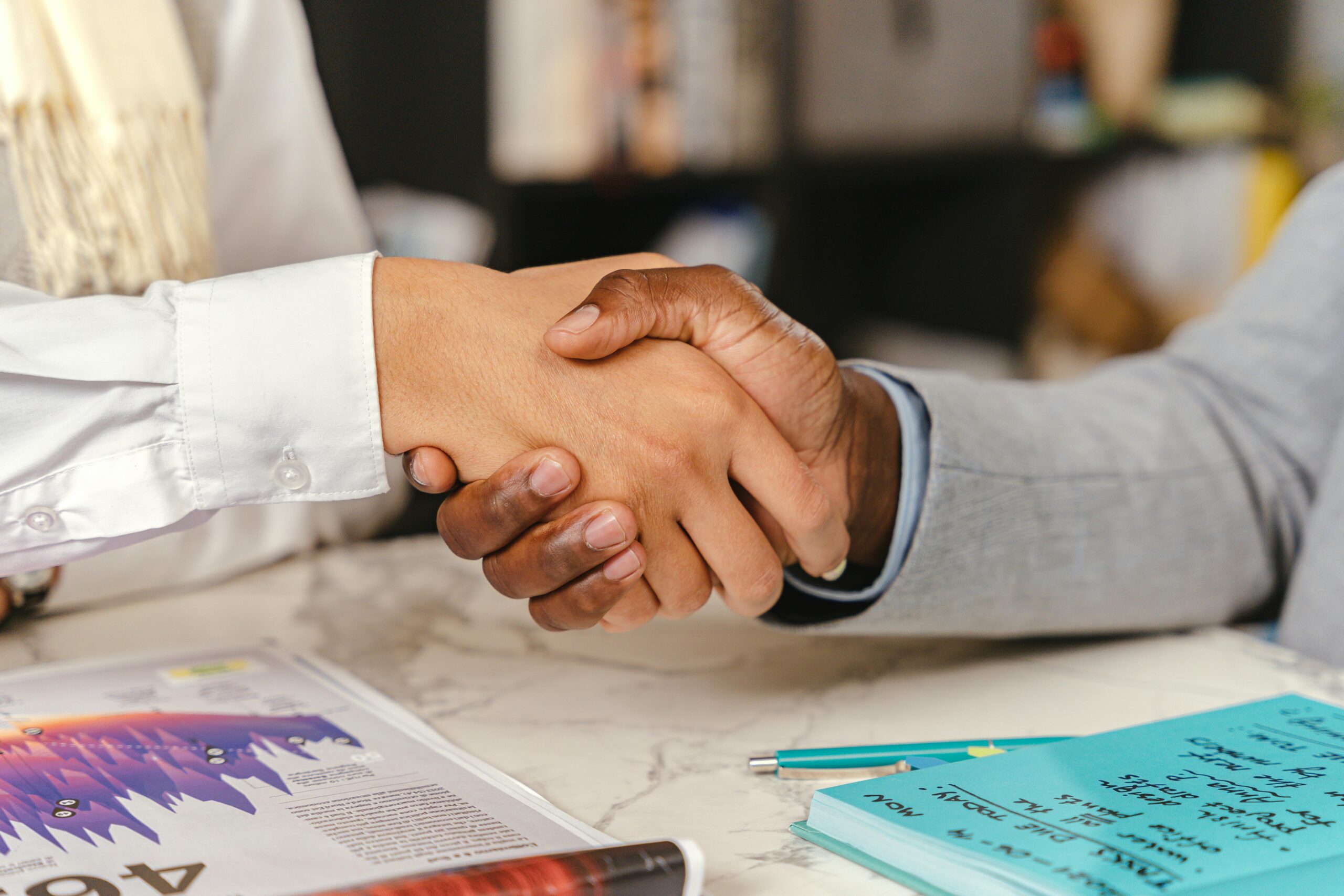 Close-up of a business handshake between two professionals over an office desk with documents.